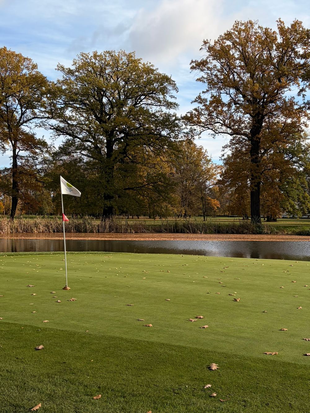 Golfový green s vlajkou u vodní překážky na podzim